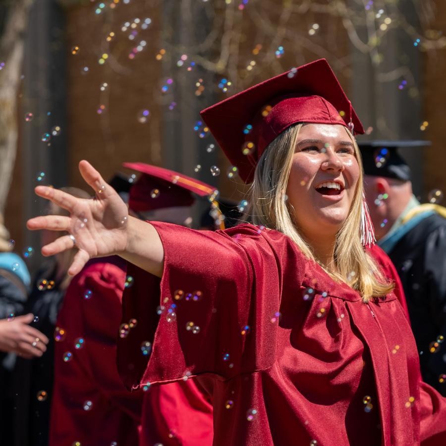 female graduate arms open while bubbles fall around her